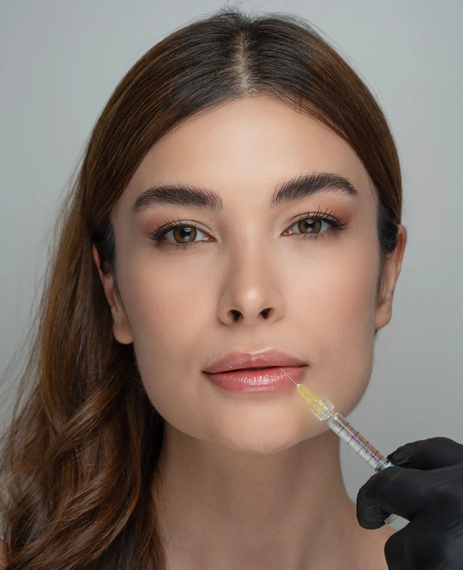 Close-up of a clinician administering a lip-area cosmetic injection in a clinical setting.