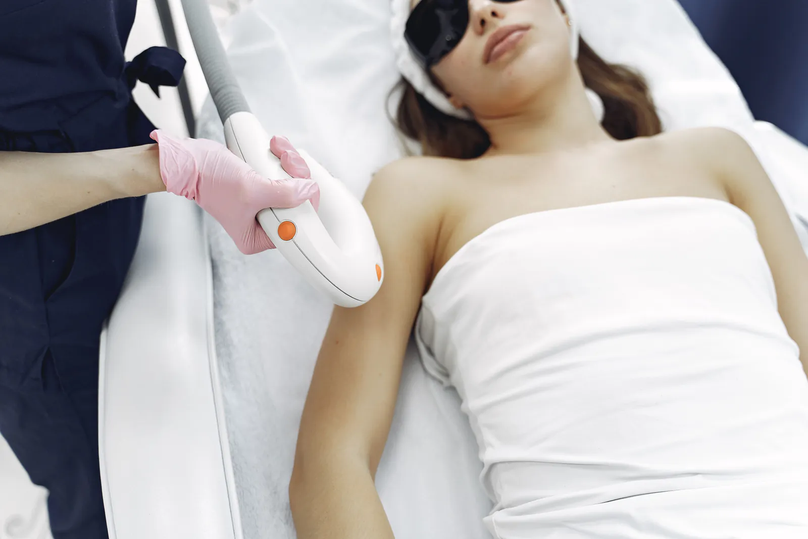 Laser hair removal treatment being performed on a client's arm while the client wears protective eyewear.